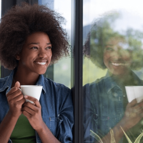 Person by glass window holding a coffee mug